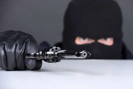 Masked robber with gun aiming into the camera against a black backgroundの写真素材