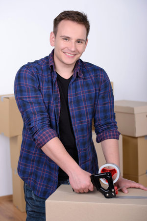 Happy man wrapping a box while he is moving home