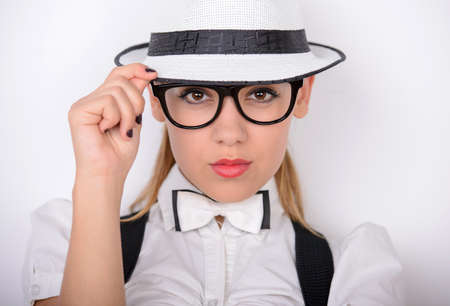 Always looking trendy. Beautiful young woman in glasses and a hat in white shirt and jeans shorts adjusting her suspenders and smilingの写真素材