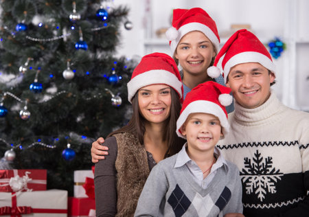 Portrait of friendly family are looking at camera on Christmas evening. Christmas Tree. Santa Hat.