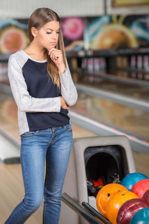 Young woman is looking at the colorful bowling balls.の写真素材