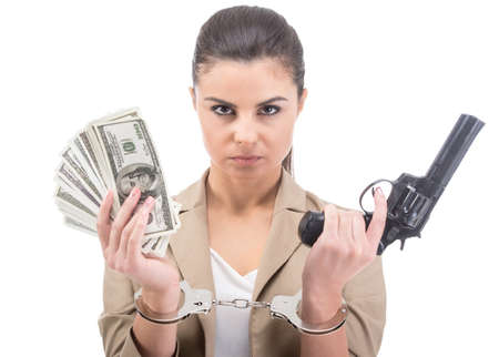 Young woman is holding in hand a lot american dollars and gun isolated on white background. A handcuffs on her hands.の写真素材