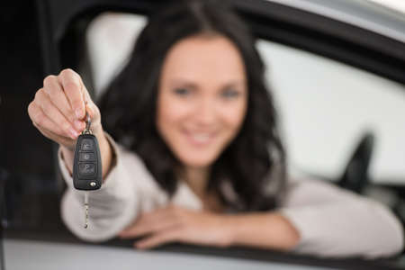 Happy young woman is holding keys to new car and looking at the camera. Focus on keys.の写真素材