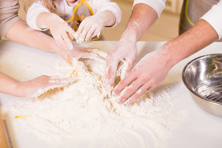 Close-up hands of family are baking cakes in home kitchen.
