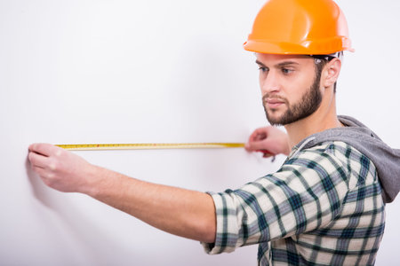 Builder in helmet with a tape measure on a white background.の写真素材