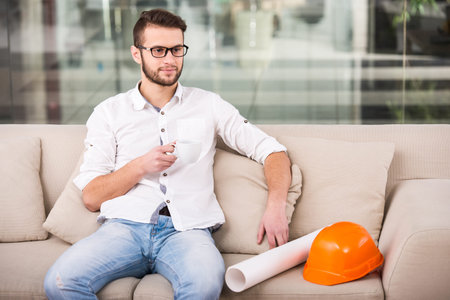 Portrait of architect with blueprint is drinking coffee while siting on the couch.の写真素材