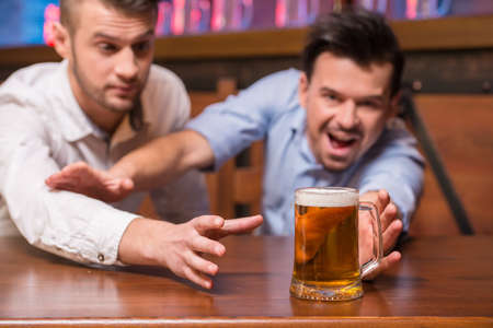 Two cheerful young men in shirt with beer while sitting together at the bar counter.の写真素材