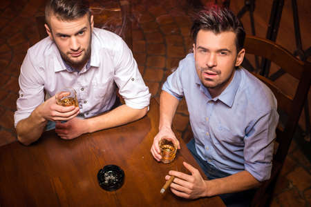 Top view of two young men are drinking whisky and smoking cuban cigar.の写真素材