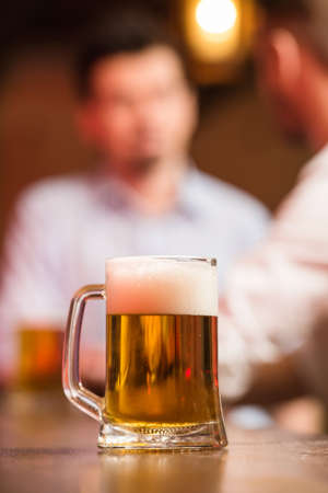 Two male friends in a pub with glasses of beer. Focus on a glass of beer.の写真素材