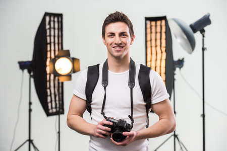 Young smiling photographer with camera in professionally equipped studio.の写真素材