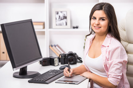 Young pretty woman is sitting at the table with pc and camera.の写真素材