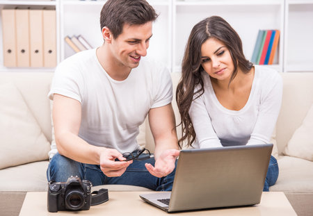 Young couple are looking at photographs on laptop.の写真素材