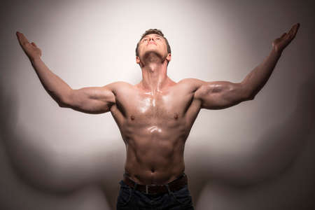 Beautiful young man shirtless is standing with hands raised isolated on white background.の写真素材