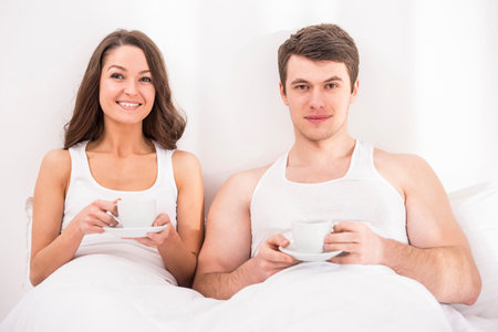 Smiling young couple having breakfast in bed. Looking at camera.の写真素材