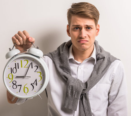 Handsome man in casual wear holding big  alarm clock on grey background.の写真素材