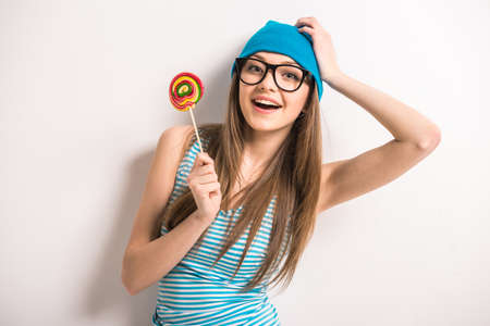 Beautiful young woman is holding lollipop and smiling while standing against grey background.の写真素材