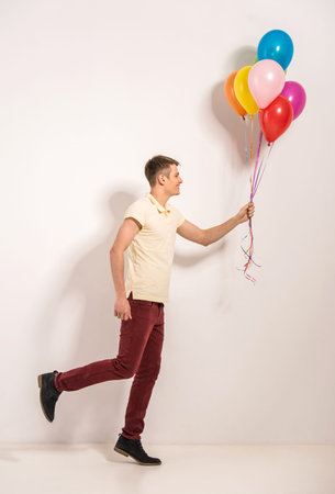 Young man with colorful balloons standing on grey background.の写真素材