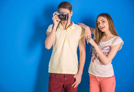 Beautiful couple are standing on blue background and making a photo with old camera.の写真素材
