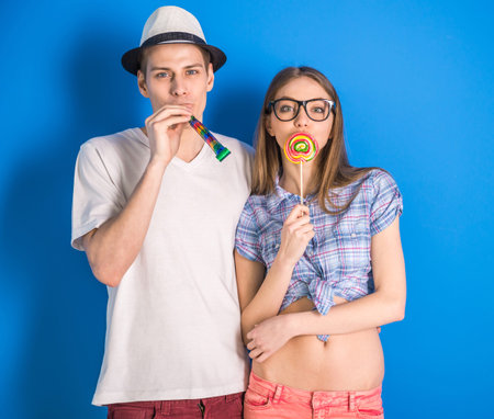 Beautiful couple having a fun together. Posing on blue background with lollipop.の写真素材