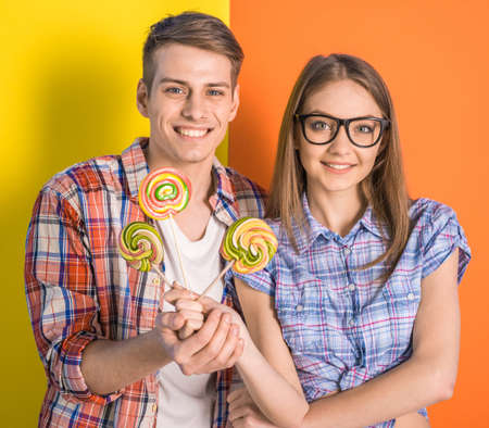 Beautiful couple having a fun together. Posing with lollipops on colorful background.の写真素材