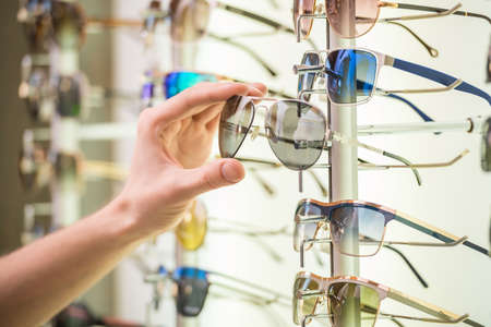 Young man (only hands) at optician with glasses is looking for sunglasses.の写真素材