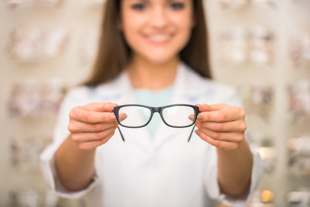 Optometrist is looking at the camera in glasses store. Professional young worker woman.の写真素材