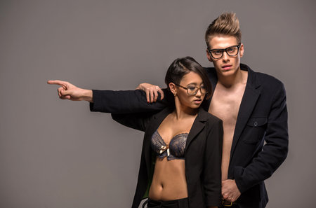 Young fashionable couple in glasses and tuxedos  posing in the studio on dark background. Fashion portrait. Passion.の写真素材