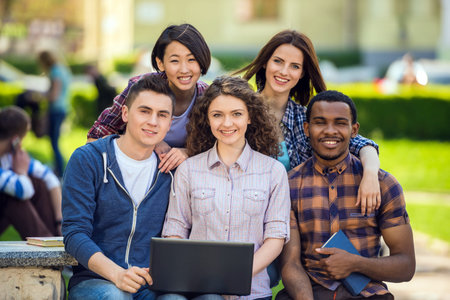 Group of young attractive smiling students dressed casual sitting on the staircase outdoors on campus at the university.の写真素材