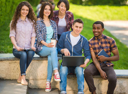 Group of young attractive smiling students dressed casual sitting on the staircase outdoors on campus at the university.の写真素材