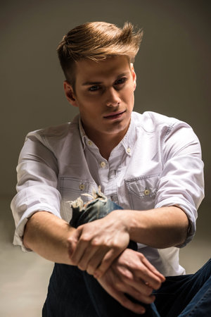 Closeup of young handsome man in shirt and jeans posing in the studio. Fashion portrait.の写真素材