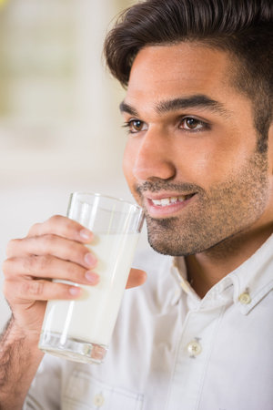 Young handsome man in white shirt drinking glass of milk for breakfast.の写真素材