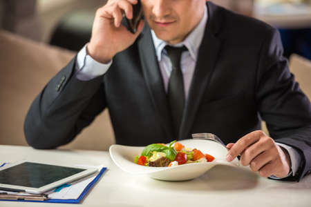 Successful businessman in suit sitting in cafe and eating salad.の写真素材