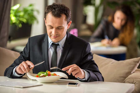 Successful businessman sitting in cafe and eating salad.の写真素材