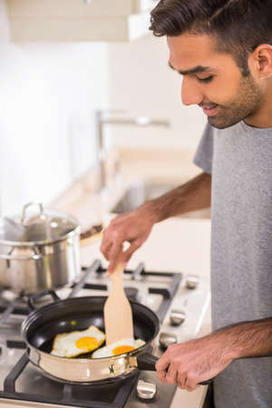 Young handsome man in grey t-shirt making omelet for breakfast.の写真素材