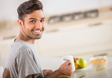 Young handsome man in grey t-shirt eating breakfast.の写真素材