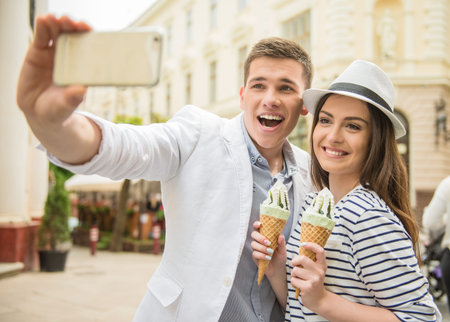 Young beautiful couple walking in the street and enjoying ice-cream. Romantic date.の写真素材