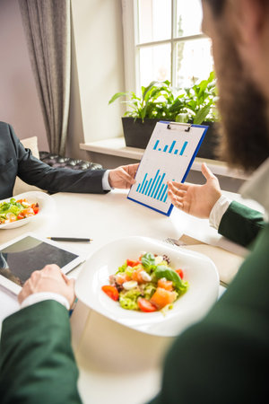 Close-up of mature business people looking at chart at business lunch.の写真素材