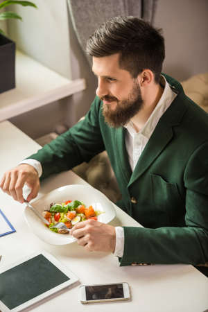 Handsome businessman sitting at the table in cafe and eating salad.の写真素材