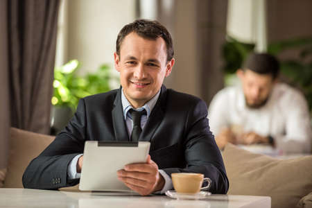 Mature handsome businessman sitting in cafe and using digital tablet.の写真素材