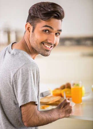 Young handsome man in grey t-shirt eating breakfast.の写真素材
