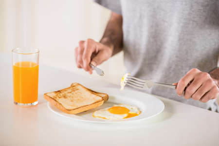 Close-up of man in grey t-shirt eating omelet and drinking juice for breakfast on white background.の写真素材