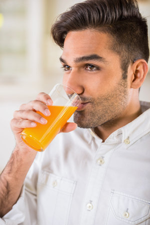 Young handsome man in white shirt drinking orange juice for breakfast.の写真素材