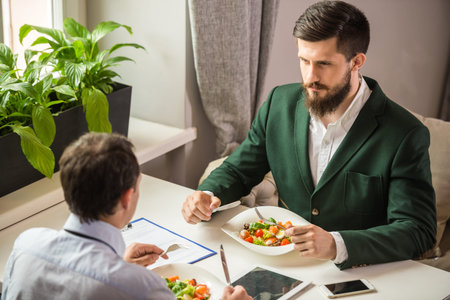 Two mature business people sitting in cafe and eating salads.の写真素材