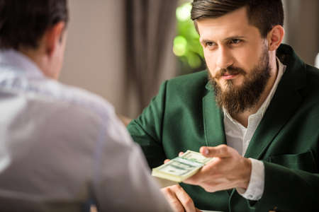 Successful businessman in suit looking at his partner and giving him money.の写真素材
