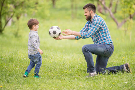Little cute boy playing football with father in summer park.の写真素材