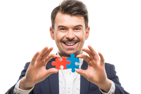 Handsome man in suit trying to connect puzzle pieces. White background.