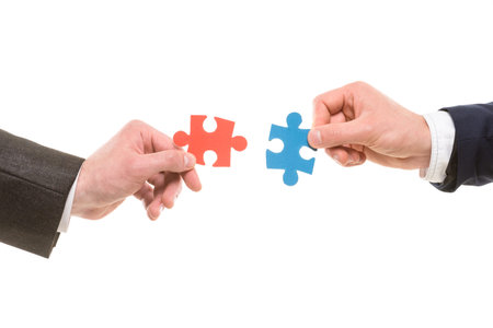 Close-up of hands trying to connect small jigsaw puzzles over white background.