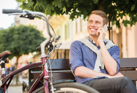 Young handsome man with bicycle sitting on the bench and resting.の写真素材