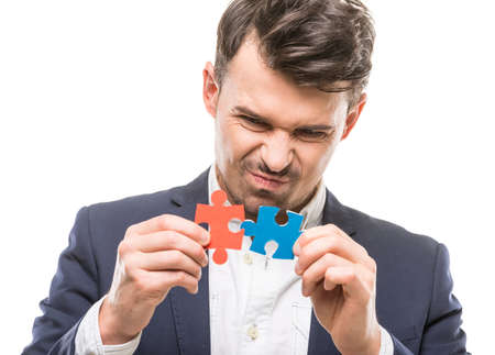 Handsome man in suit trying to connect puzzle pieces. White background.の写真素材