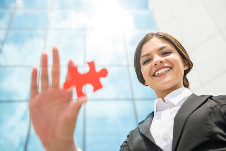 Beautiful business woman dressed formal holding puzzle. Sky background.の写真素材